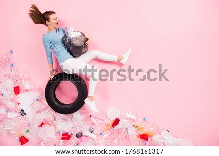 Top above high angle view full body profile side photo of happy excited girl sit tyre hold rubbish bag ride road plastic trash cup bottle glass flat lay isolated pastel color background