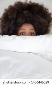 Top Above View Close Up Adorable African American Kid Hiding Under Duvet, Scared By Bad Dream. Mixed Race Afraid Child Girl Lying In Bed, Awakened By Nightmare, Peeking From Blanket, Feeling Fear.