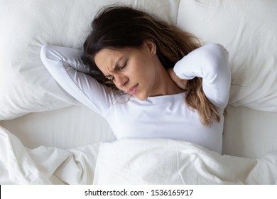 Top Above View Head Shot Close Up Stressed Young Mixed Race Woman Feeling Neck Ache, Suffering From Painful Feeling In Neck In Morning After Sleeping On Uncomfortable Pillow At Home Or Hotel Room.