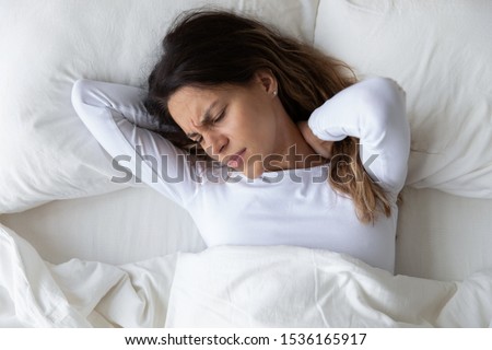 Top above view head shot close up stressed young mixed race woman feeling neck ache, suffering from painful feeling in neck in morning after sleeping on uncomfortable pillow at home or hotel room.