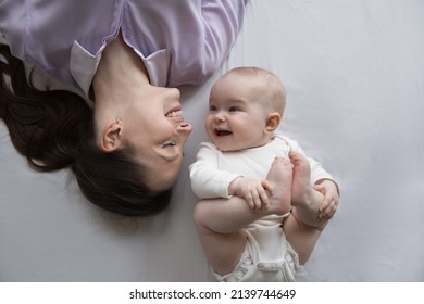 Top above view joyful young mother lying on bed with cute laughing baby boy girl, having fun after waking up in morning. New mommy communicating with few months kid son daughter, childcare concept. - Powered by Shutterstock