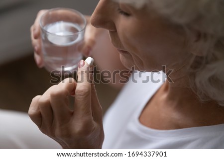 Top above view middle aged retired woman holding pill and glass of water, taking daily dose of vitamins. Elder old granny drinking painkillers, suffering from headache or painful feelings at home. Foto d'archivio © 