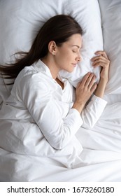 Top above view vertical image tranquil young brunette woman in pajamas lying under duvet on comfortable orthopedic mattress, sleeping on soft pillow, enjoying sweet dreams good night rest in bed.