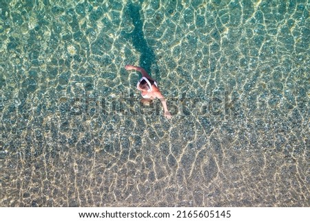 Top, aerial view. Athletic body of young beautiful woman in headphones listening music walking in bikini in sea water on the sand beach. Drone, copter photo. Summer vacation.
