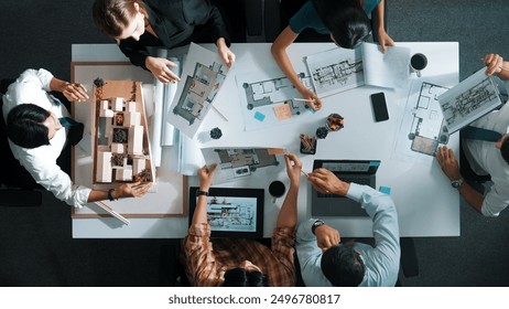 Top aerial view business people brainstorming about building interior at table with house model and laptop displayed house plan while architect engineer drawing and writing at blueprint. Alimentation. - Powered by Shutterstock