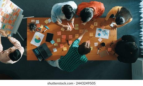 Top aerial view of diverse team writing colorful sticky notes to brainstorm marketing idea while looking at financial chart. Top view of smart business people taking a note about plan. Convocation. - Powered by Shutterstock