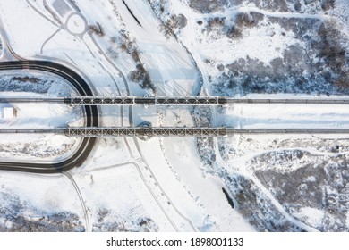 Top Aerial View Of The Railway Bridge Over The Frozen River Covered With Snow On A Winter Sunny Day.