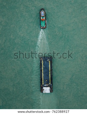 Top aerial view of a tug boat towing an empty barge taken on a drone