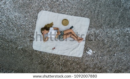 Top aerial view of a woman on the beach in shorts and a vest on a beach towel. Photo from drone.