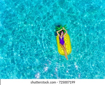 Top aerial view of a woman swimming with inflatable mattress in a pineapple shape. On holidays having fun and relaxing at the beach.
