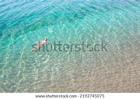 Top, aerial view. Young beautiful woman in white bikini swimming in sea water on the sand beach. Drone, copter photo. Summer vacation. View from above. 