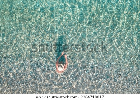 Top, aerial view. Young beautiful woman in a hat and white bikini swimming in sea water on the sand beach. Drone, copter photo. Summer vacation. View from above. 