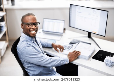 Top African-American Tax Advisor Smiling While Multitasking at His Desk in a Corporate Office. Professional Accountant Analyzing Financial Data. - Powered by Shutterstock