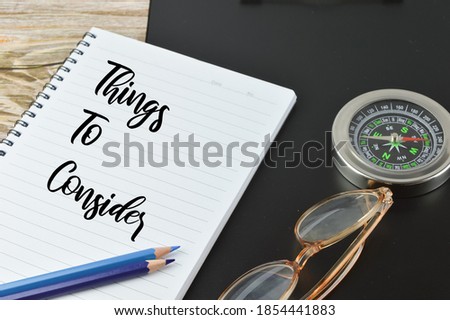 Top angle view of paper holding file, compass, glasses, colors and notebook written with text THINGS TO CONSIDER. Business and education concept. 