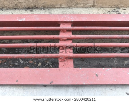 Top angle view of a rusty red metallic gutter cover installed over a narrow water channel.