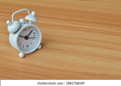 Top angle view of white clock over wooden background. Copy space for the text. 