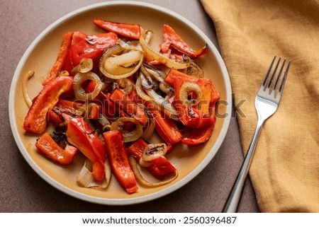 Top angle view of a yellow ceramic plate with shakshuka bell peppers and onions with linen napkin and metal fork on the side