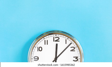 Top of big plain wall clock on pastel blue background. Five past twelve o'clock. Top view copy space, time management or school concept and summer or winter time change, opening hours, lunch break