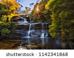 Top cascade of WEntworth falls flowing to Valley of Waters high in Blue Mounains national park in the morning against rising sun through lush leaves of gum trees.