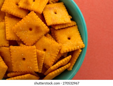 Top Close View Of A Bowl Of Cheese Crackers Atop An Orange Background Illuminated With Natural Light.