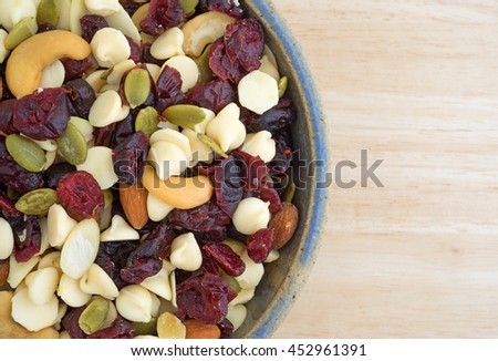 Top close view of a bowl full of an assortment of nuts and dried cranberries trail mix on a wood table top.