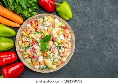 Top Close View Of Bowl Of Vegetable Salad With Carrots Greens And Bell Peppers On Side On Dark Grey Table