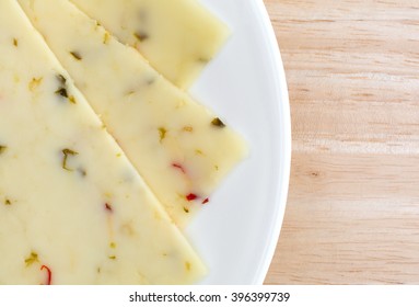 Top Close View Of Pepper Jack Cheese Slices On A White Plate Atop A Wood Table Top.