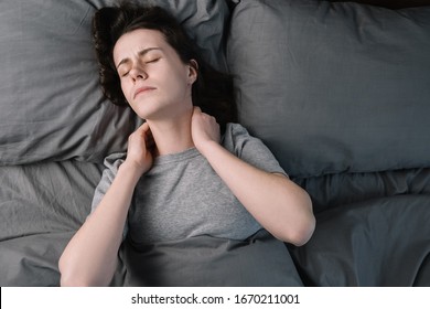 Top Close Up View Upset Young Woman Lying In Bed In Morning Feels Pain In Neck After Night Sleep, Awaken Having Painful Sudden Ache Or Stiffness, Incorrect Posture During Sleep. Fibromyalgia Concept