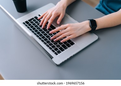 Top close-up view of hands of unrecognizable business woman typing on laptop keyboard sitting at desk with coffee cup in home office, selective focus.