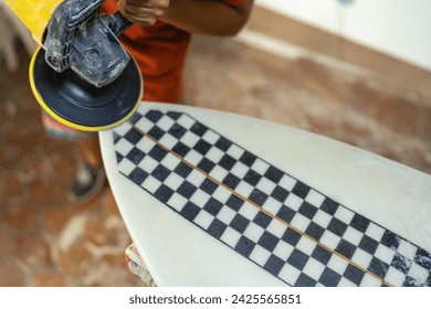 Top close-up view of a man using an electric disc to polish a surfboard