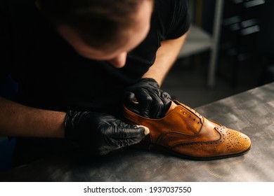 Top close-up view of professional shoemaker wearing black gloves polishing old light brown leather shoes. Concept of cobbler artisan repairing and restoration work in shoe repair shop. - Powered by Shutterstock