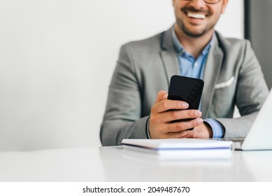 Top Cut Portrait Of A Cheerful Man Using Smart Phone At Home, Or Cellphone At Office Desk. Small Business Entrepreneur Looking At His Mobile Phone And Smiling.