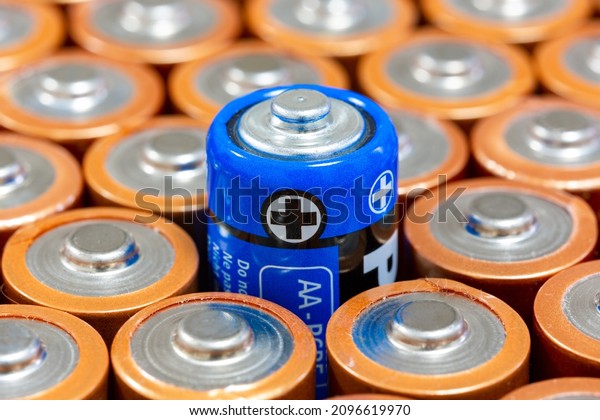 Top\
diagonal view of the positive poles of 1.5 V AA Alkaline batteries.\
Battery with blue outer layer coating in selective focus. Above the\
blue plated battery values. Differences\
concept.
