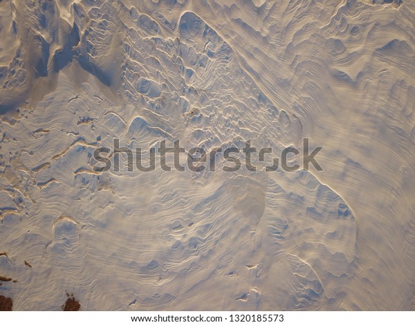 Top down aerial drone footage\
of a snow field.  It looks like the surface of another\
planet.