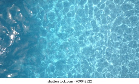 Top down aerial drone image hovering over a backyard swimming pool with waves glimmering in sunlight.
