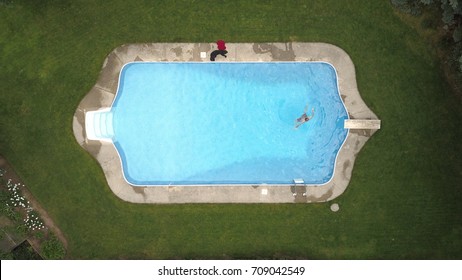 Top Down Aerial Drone Image Of A Backyard Swimming Pool Surrounded By Turfgrass With A Swimmer In The Deep End.