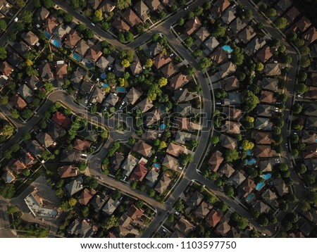 Top down aerial drone image of a suburb in the midst of summer, backyard turf grass and trees lush green.  The roofs and pools look colorful.