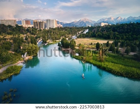 Top down aerial drone shot of Man at stand up paddle boards SUP in the river and mountain lake Sairan in city Almaty in Kazakhstan.
