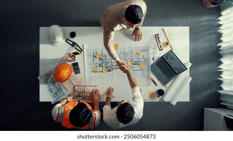 Top down aerial view of architect engineer team shake hands and discussing about building construction. Group of diverse people working together to plan and design by using blueprint. Alimentation. - Powered by Shutterstock