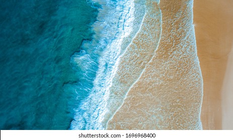 Top down aerial view of beach with waves crashing into the sand during day time