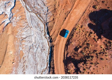 Top down aerial view of a bright blue SUV driving off-road though rough desert landscape with red sand and rocks.