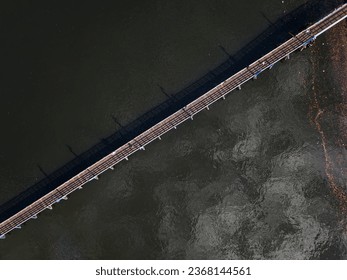A top down, aerial view of a footbridge over Sheepshead Bay, Brooklyn during a sunny day with people walking on the bridge. Taken by a drone camera, directly over the calm waters. - Powered by Shutterstock