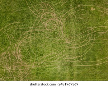 A top down aerial view over a grass field with tire tracks and skid marks. Taken on a sunny day with a drone camera. - Powered by Shutterstock