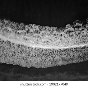 Top down aerial view of sea wave and foam in black and white. Ocean water and beach background with motion blur.