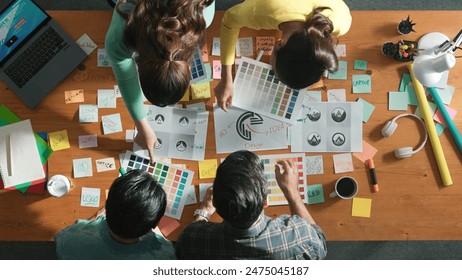 Top down aerial view of skilled designer hold logo while discuss with team. Aerial business group working together sharing idea about logo graphic design by using sticky notes and tablet. Symposium. - Powered by Shutterstock