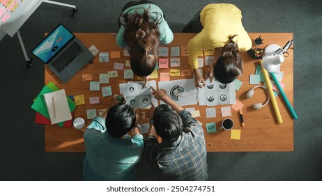 Top down aerial view of skilled designer hold logo while discuss with team. Aerial business group working together sharing idea about logo graphic design by using sticky notes and tablet. Symposium. - Powered by Shutterstock