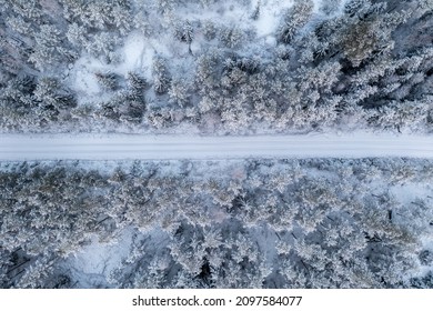 Top down aerial view of snow covered forest and road in winter. Snowy trail in taiga forest.