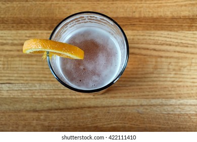 Top Down Angle Perspective Of Beer In Glass With Lemon Orange Wedge On Rim Sitting On Wood