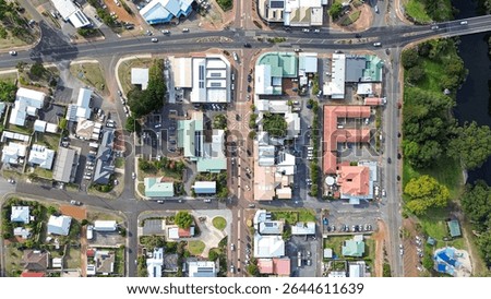Top down Arial view of a small rural town centre with cars on the road, roof tops of homes and businesses, a river with park and trees. Main road with 4 Way intersection. Denmark Western Australia 