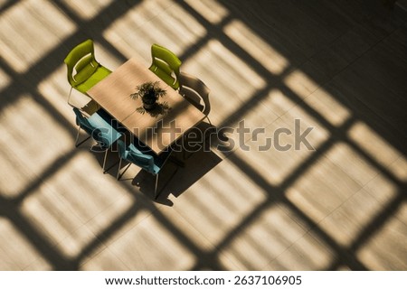 A top down bird's eye view of a public table is seen inside a building under the shadow of a glass roof. 